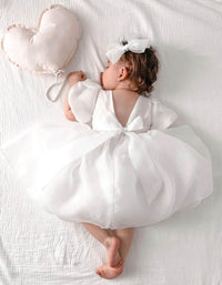 Cleo organza flower girl dress with puff sleeves is worn by a baby flower girl, she also wears a tulle bow in her hair.