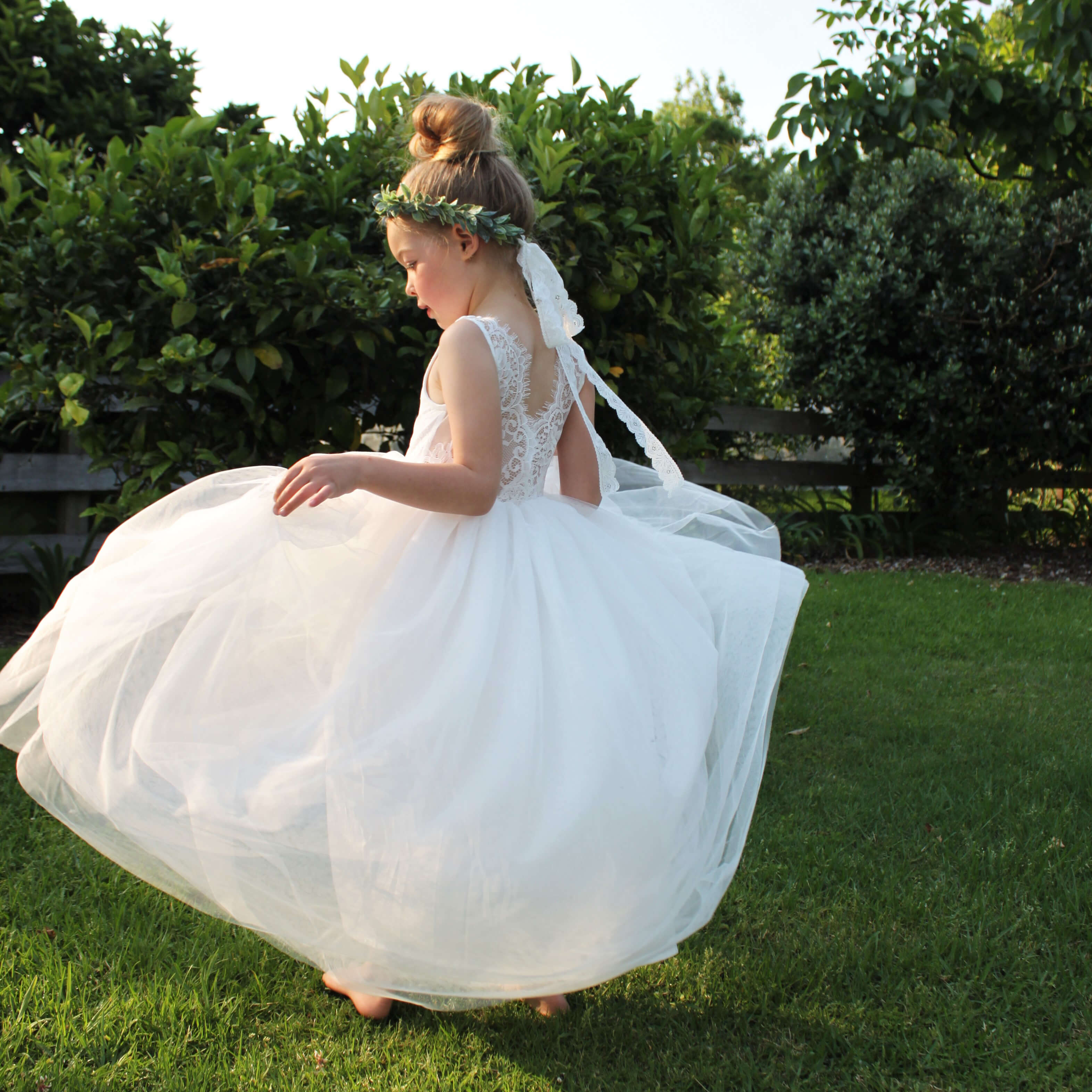 Young girl twirls wearing our Mia flower girl dress, showing the beautiful tulle skirt twirling and the detailed lace back.