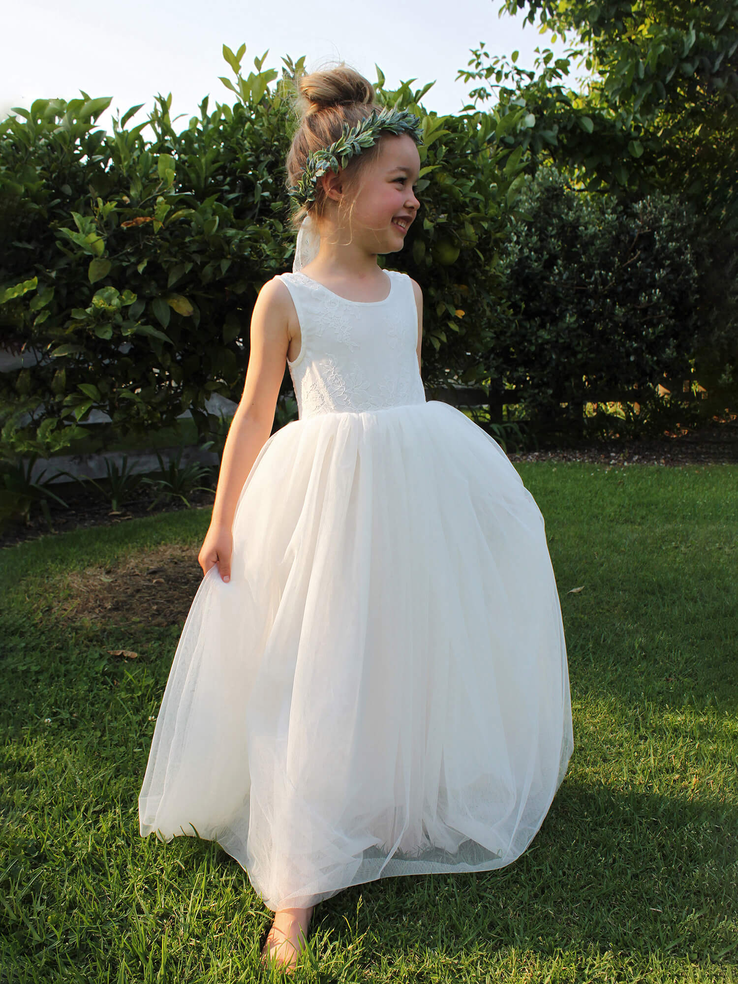Mia flower girl dress being worn by a girl. Showing the full tulle skirt and sleeveless lace bodice. She also wears our Olive flower crown.