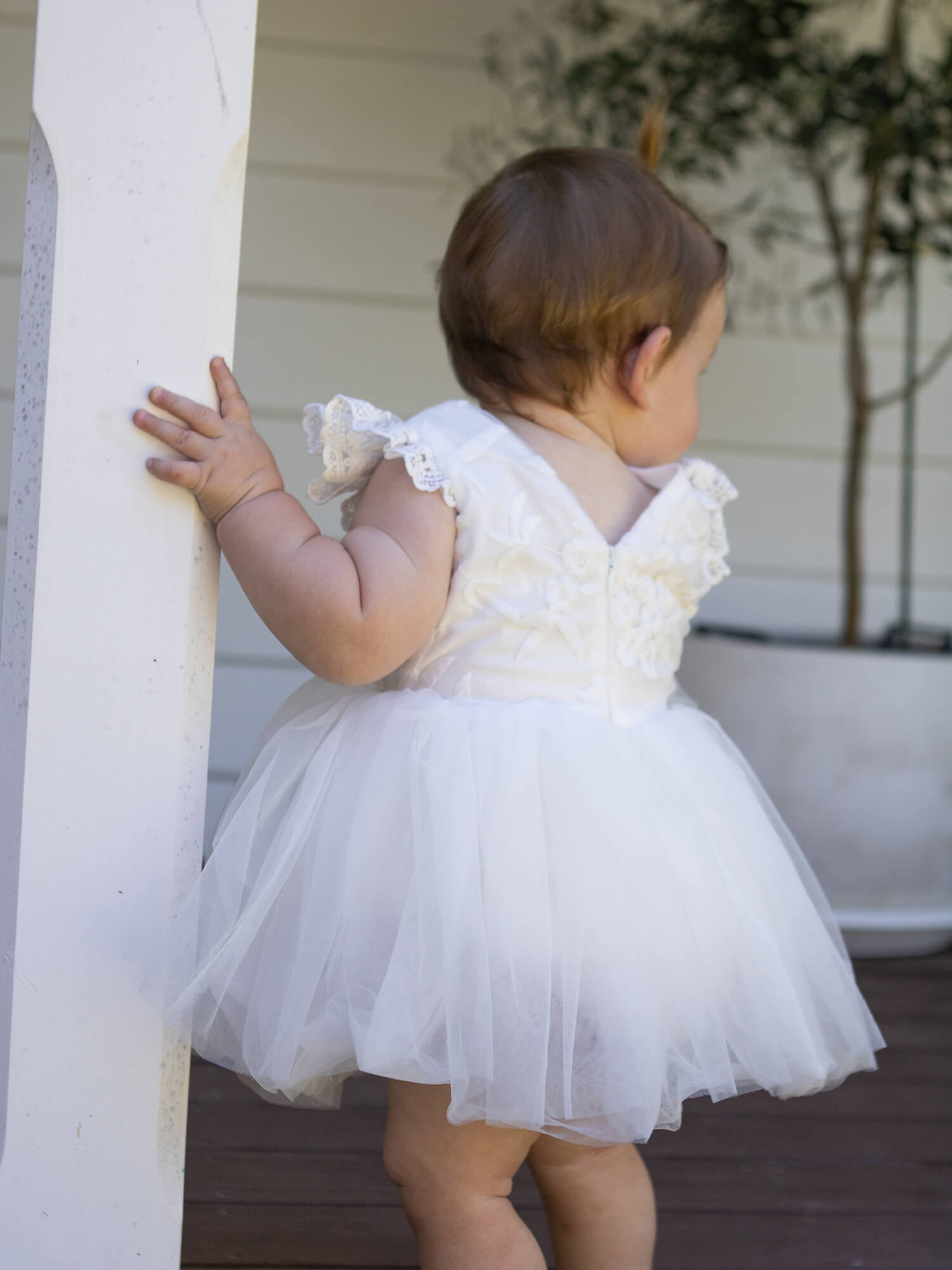 A baby wears our Abigail lace and tulle baby flower girl romper in ivory.
