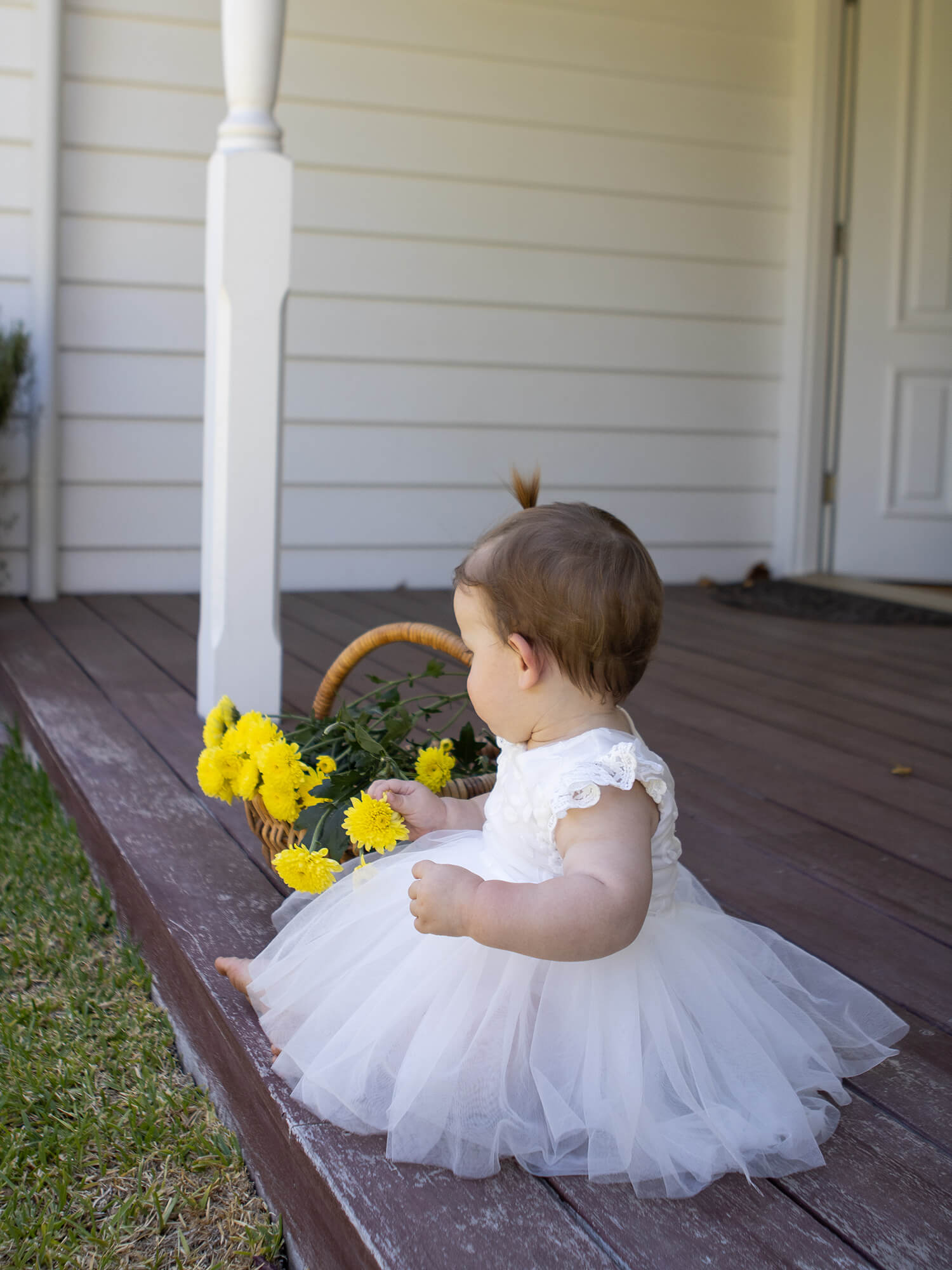 Abigail lace baby flower girl romper is worn by a baby who is sitting playing with a basket of flowers.