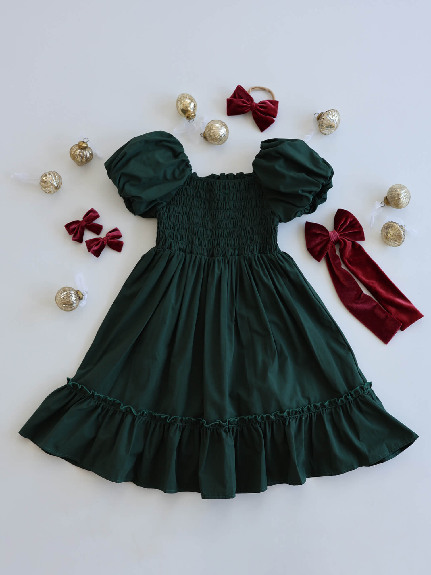 Ava emerald green Christmas dress with shirring at the back for stretch, surrounded by Christmas decorations and matching accessories.