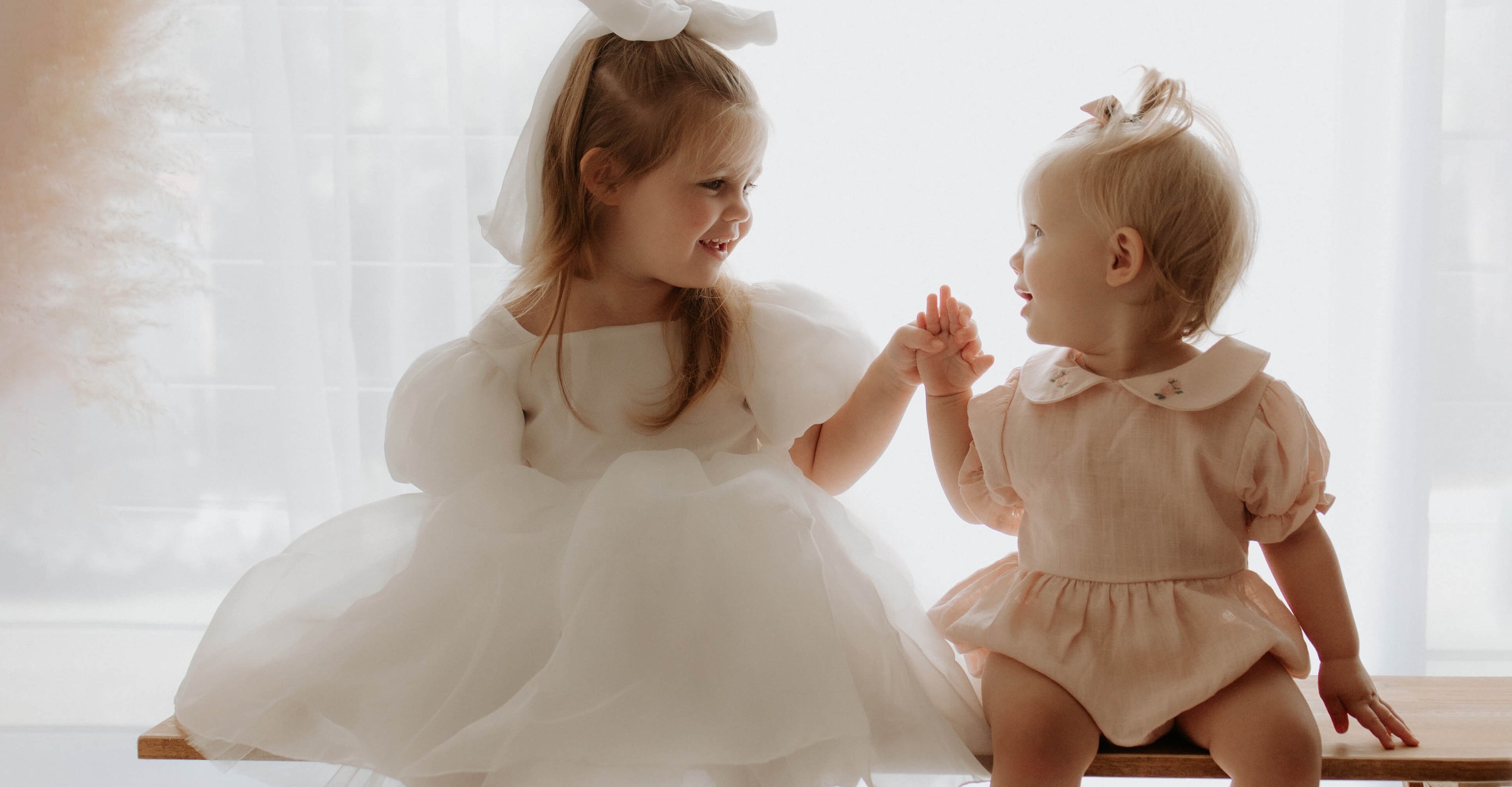 Flower girl wears our Cleo puff sleeve flower girl dress, sitting with her baby sister who wears our Emma romper.