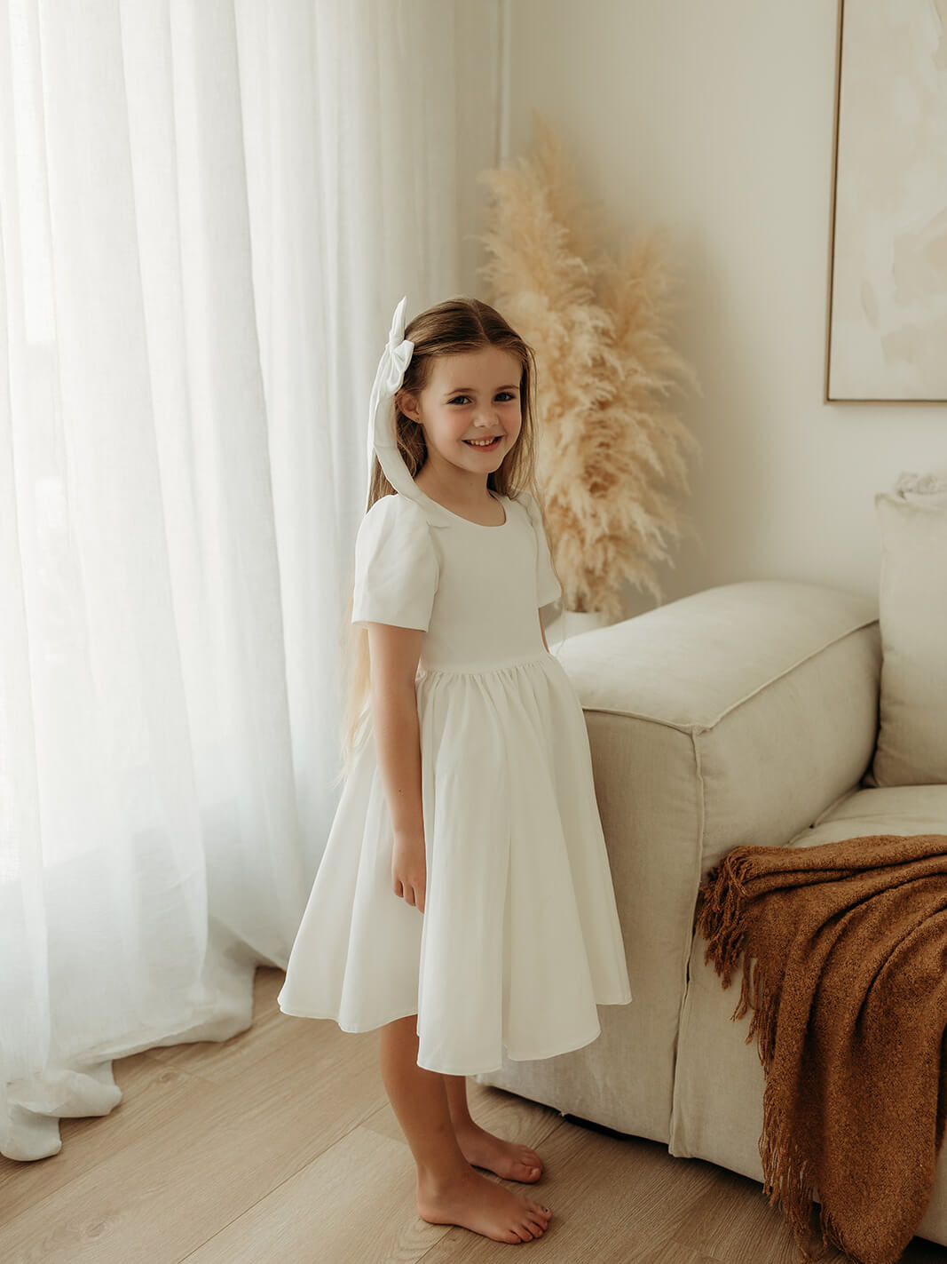 A little girl wears our Charlotte flower girl dress in white crepe, along with our satin hair bow.