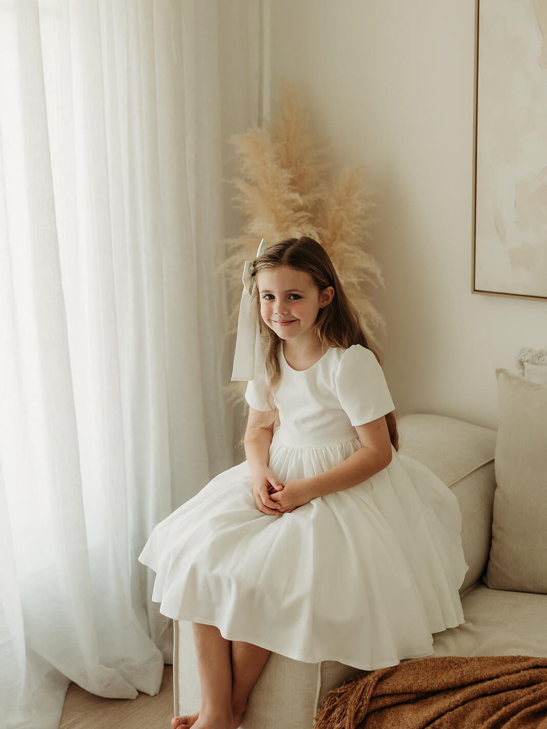A little girl smiles as she sits wearing our Charlotte crepe flower girl dress.