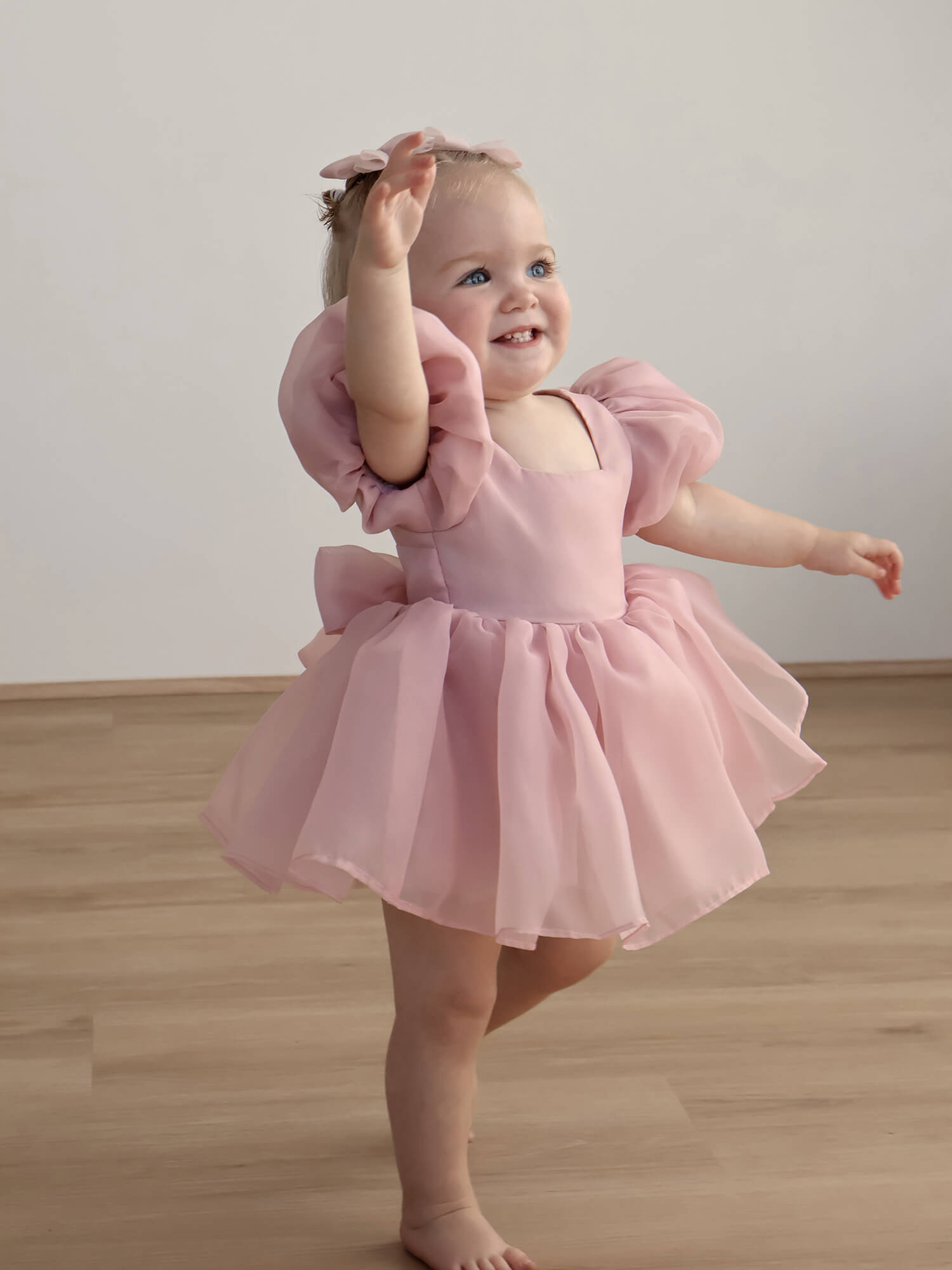 A toddler wears our Cleo puff sleeve baby romper in blush organza.