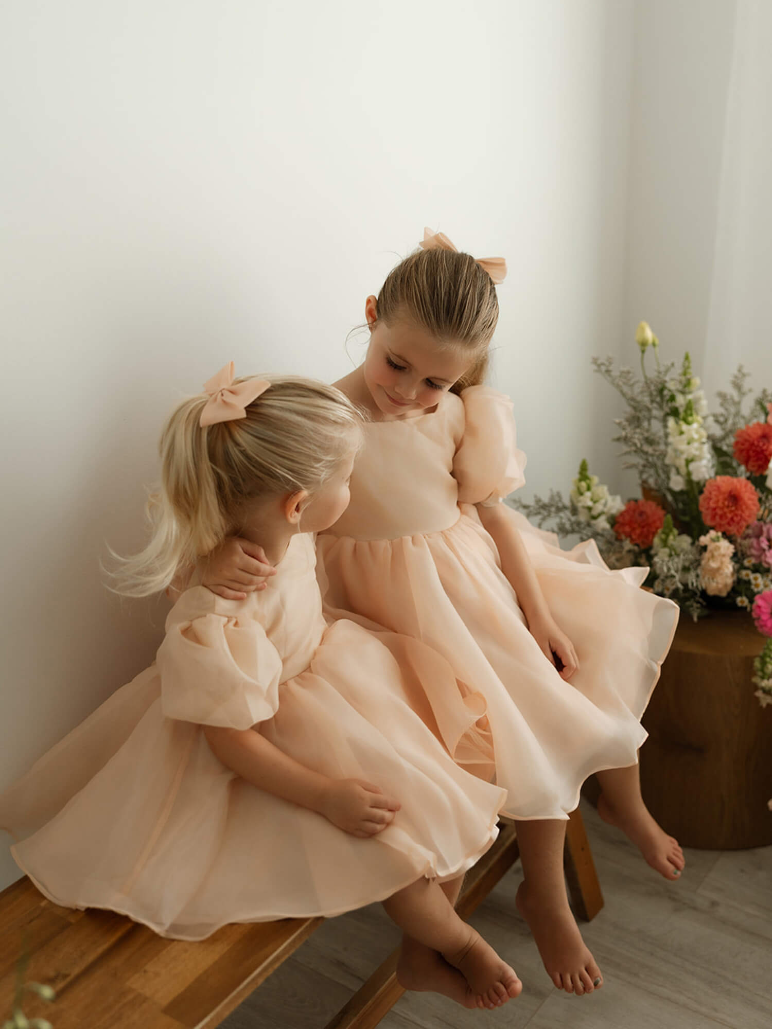 Two sisters wear our Cleo champagne puff sleeve flower girl dress.