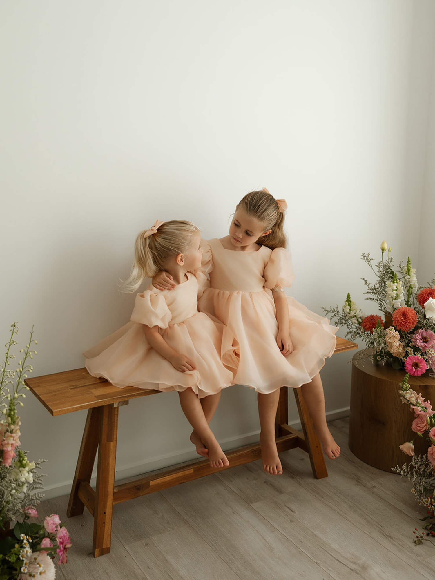 Matching sisters wear our Cleo champagne flower girl dress and champagne organza bow clips.