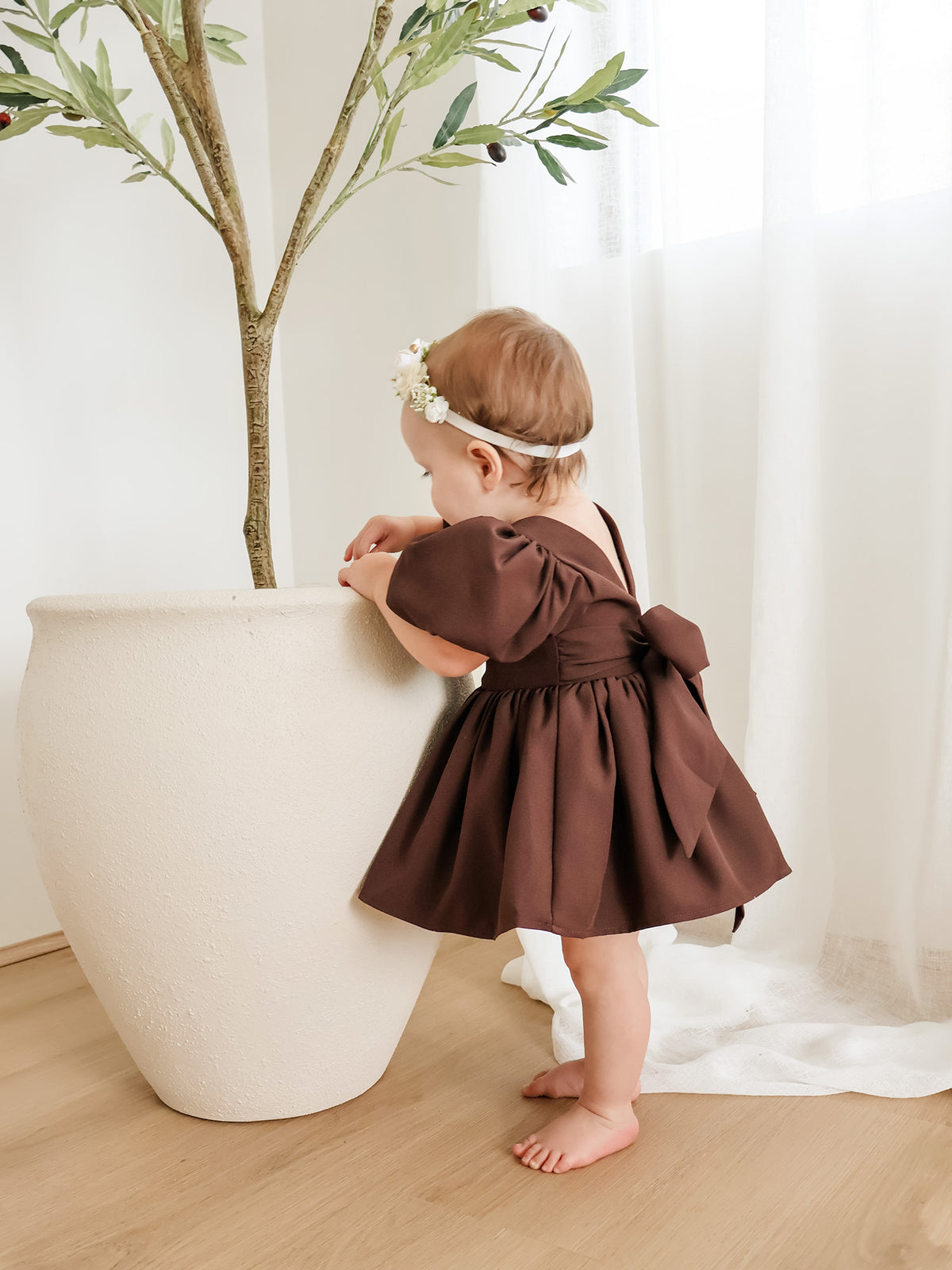 Cleo chocolate crepe puff sleeve flower girl romper for babies is worn by a baby girl.