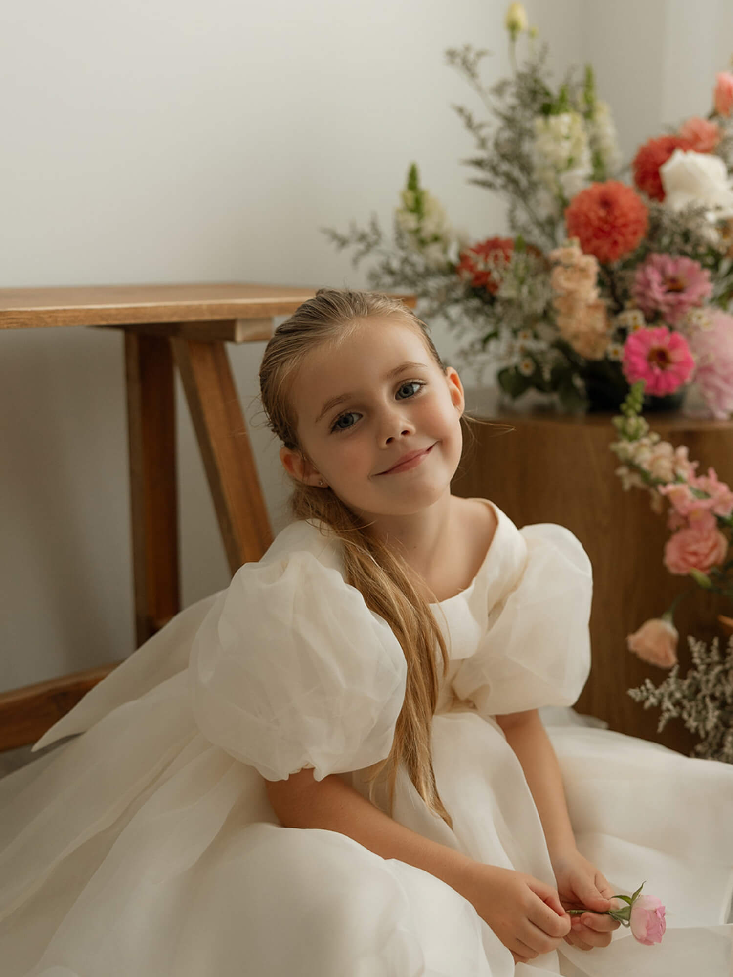 The Cleo dress in cream organza, a whimsical and classic flower girl outfit for weddings, is worn by a young girl.