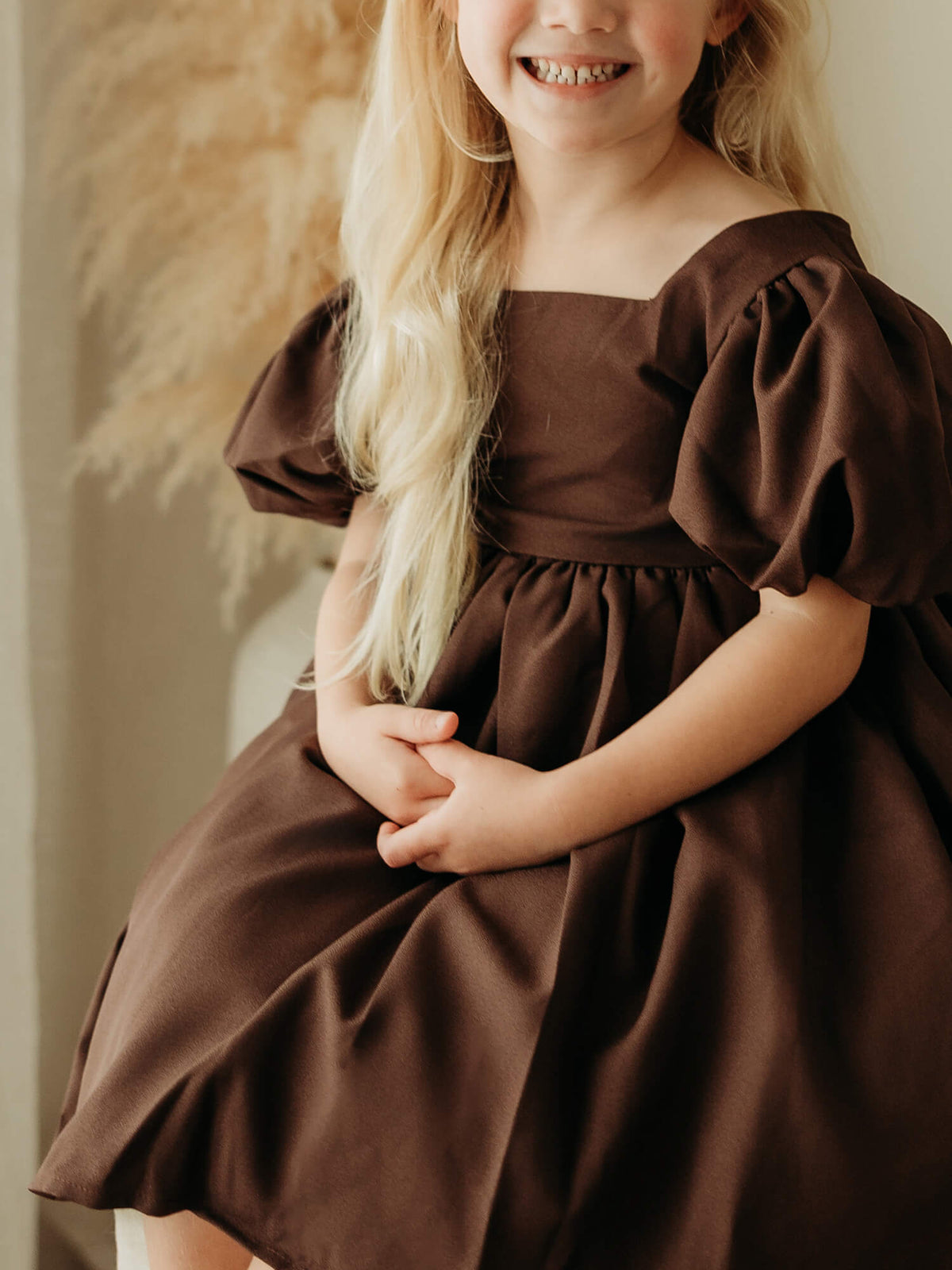Cleo flower girl dress in chocolate crepe is worn by a young girl, showing the puff sleeves and crepe fabric.