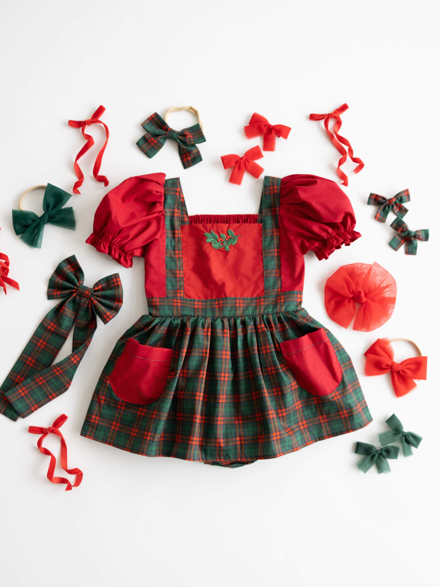 Red and green tartan baby romper with puff sleeves and holly embroidery.