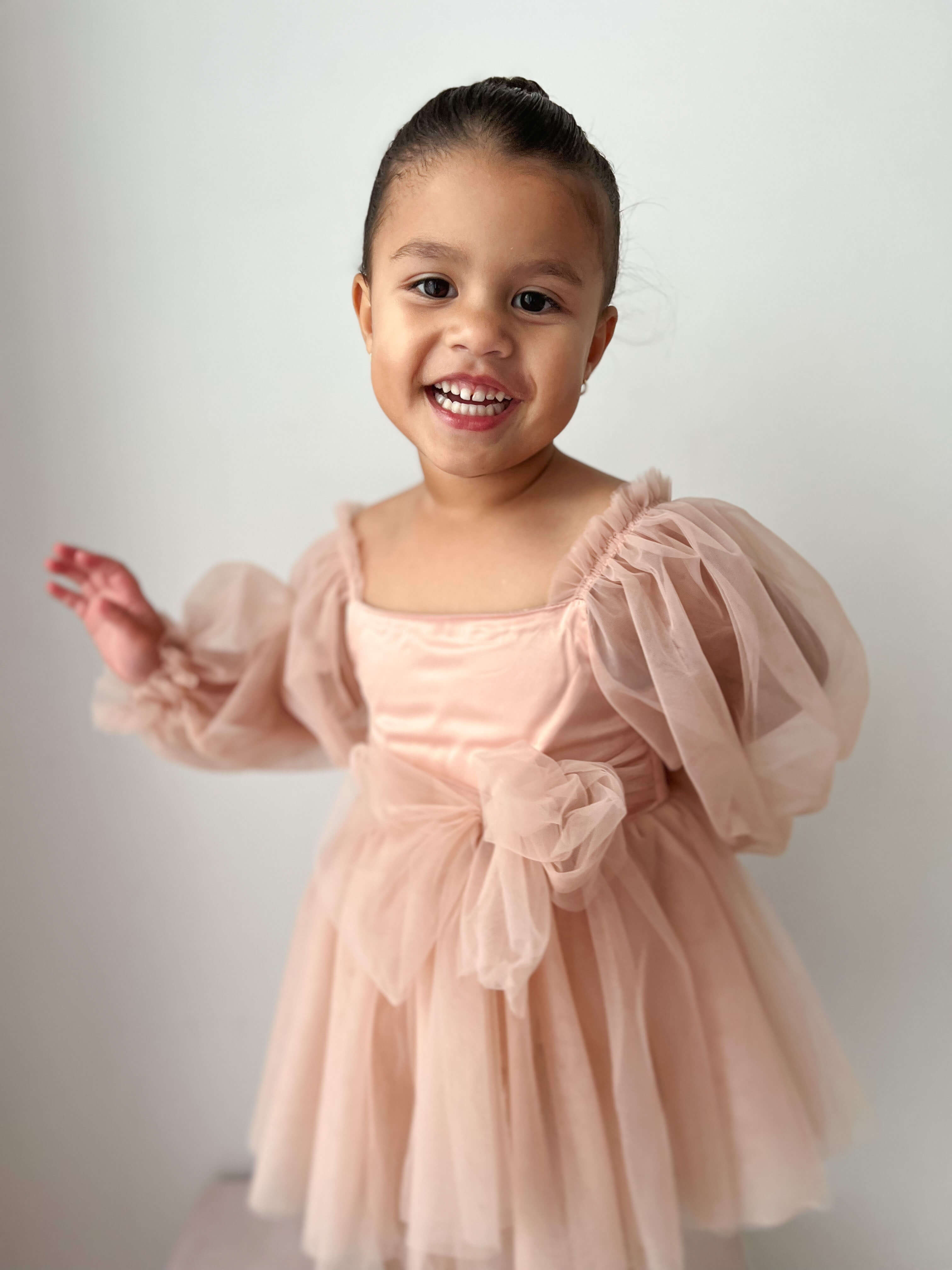 A little girl smiles wearing our champagne Eva flower girl dress for babies and toddlers.
