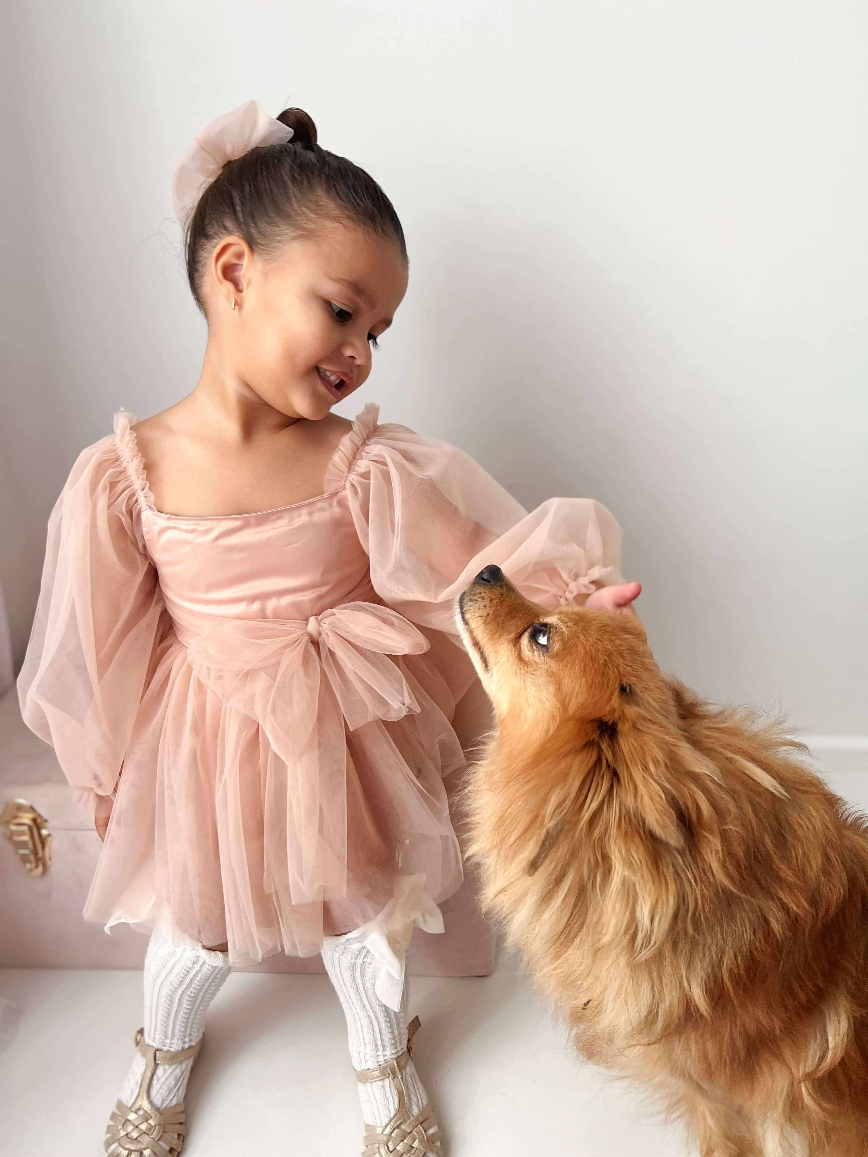 A little girl stands petting a dog, she wears our champagne Eva flower girl romper and matching champagne tulle bow hair clip.