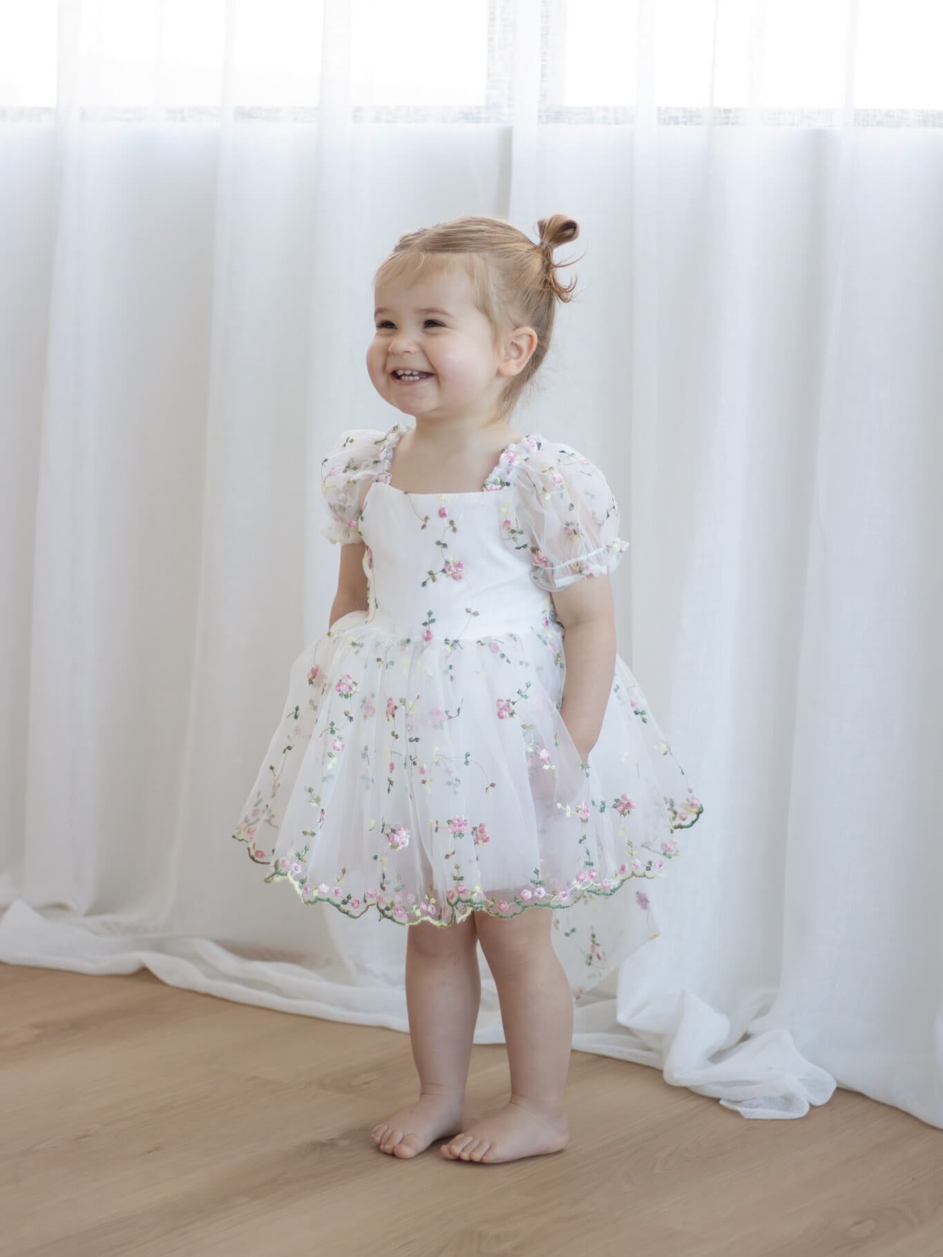 A toddler smiles wearing our Fleur meadow flower girl romper in meadow pink.