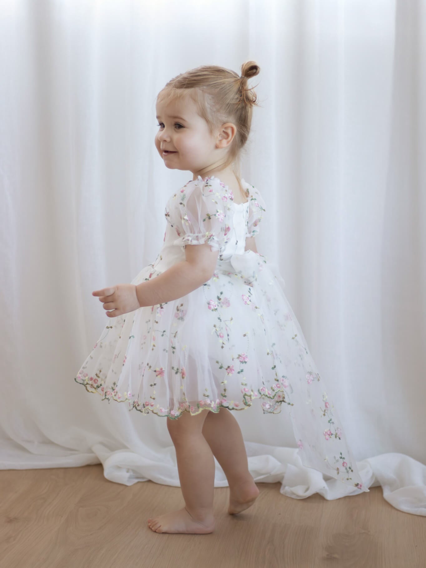 Fleur meadow pink flower girl romper is worn by a toddler, showing the organza bow at the back.