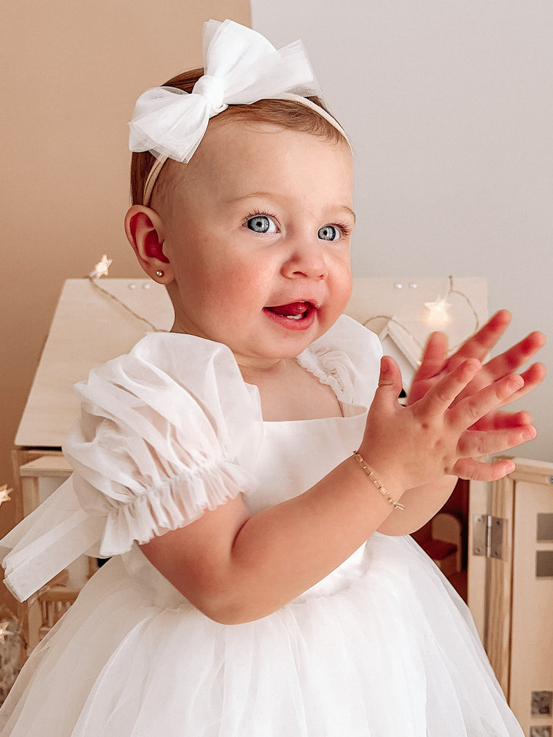 Gabrielle baby flower girl dress is worn by a young baby along with a tulle bow headband.