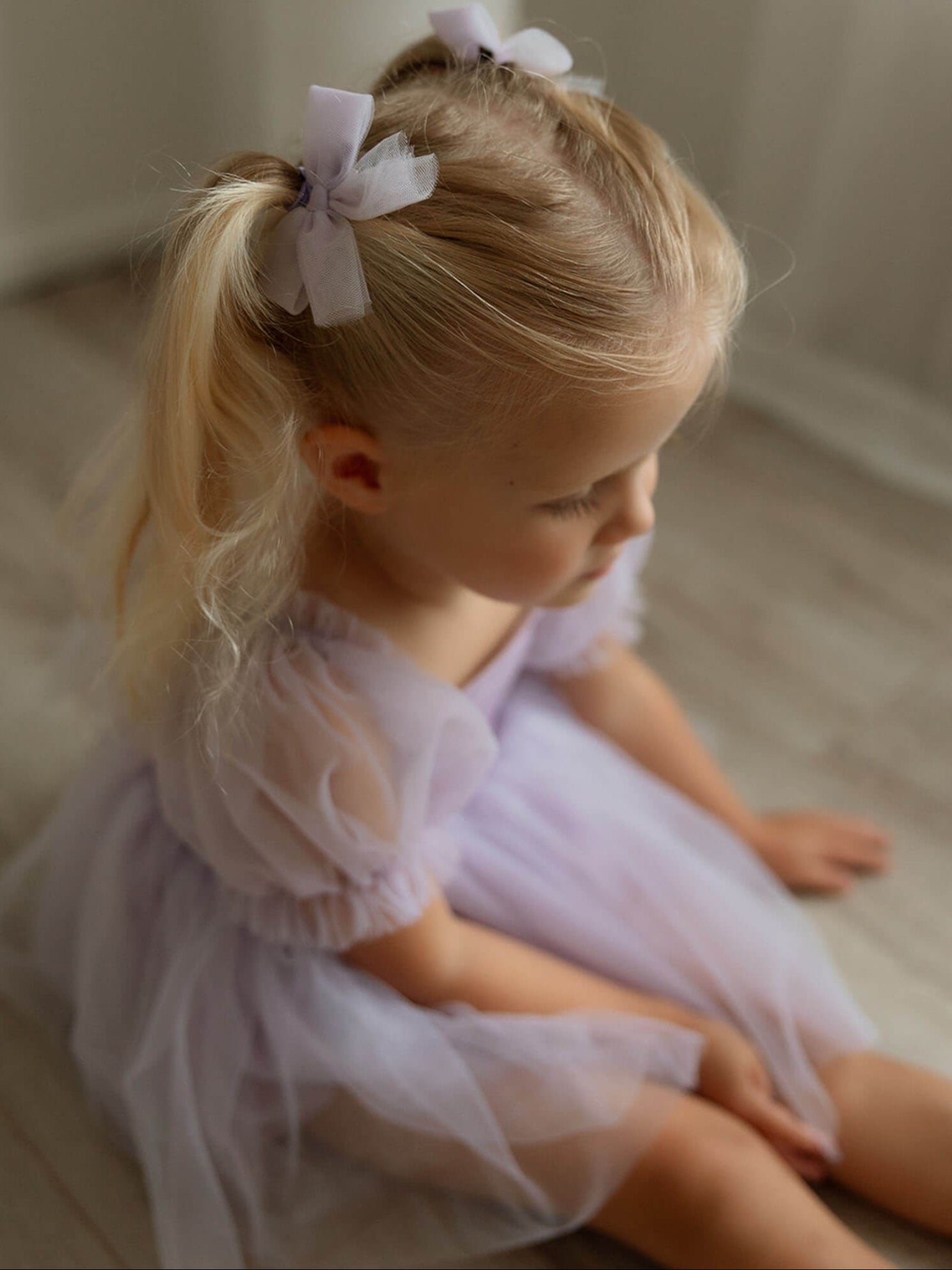 Gabrielle lilac purple flower girl romper and matching lilac tulle pigtail hair clips are worn by a toddler.