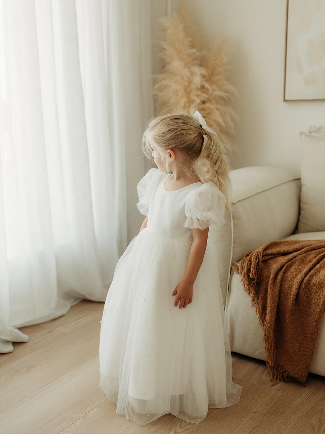 A little girl wears our Gracie full length tulle flower girl dress with peal beading.