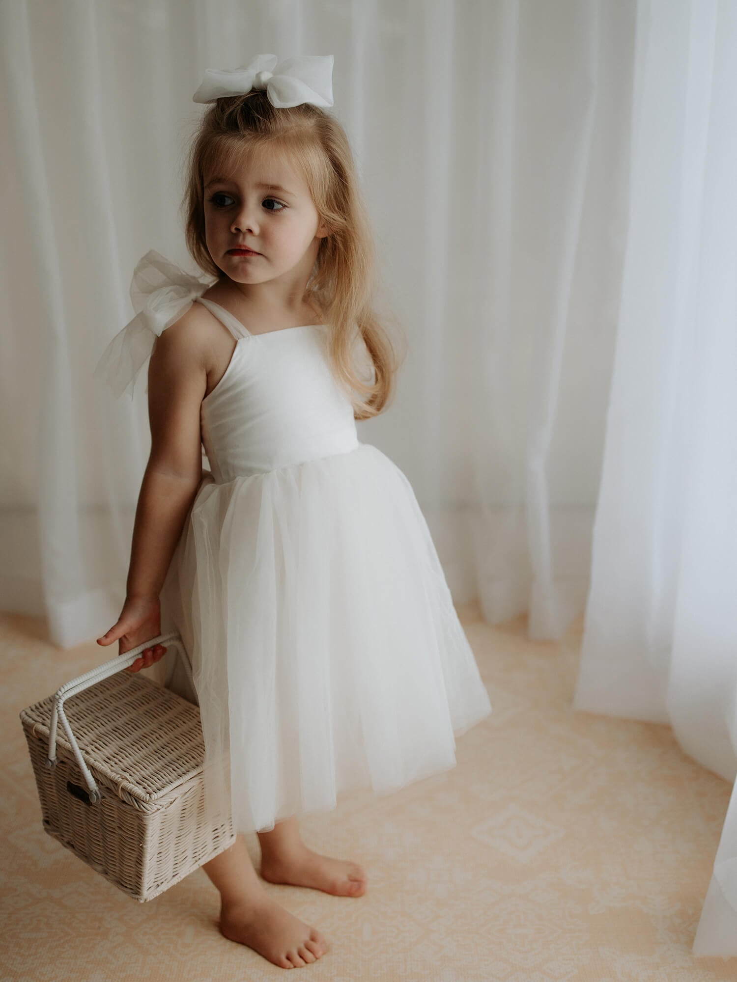 Harper tea length flower girl dress in cream is worn by a girl carrying a basket.