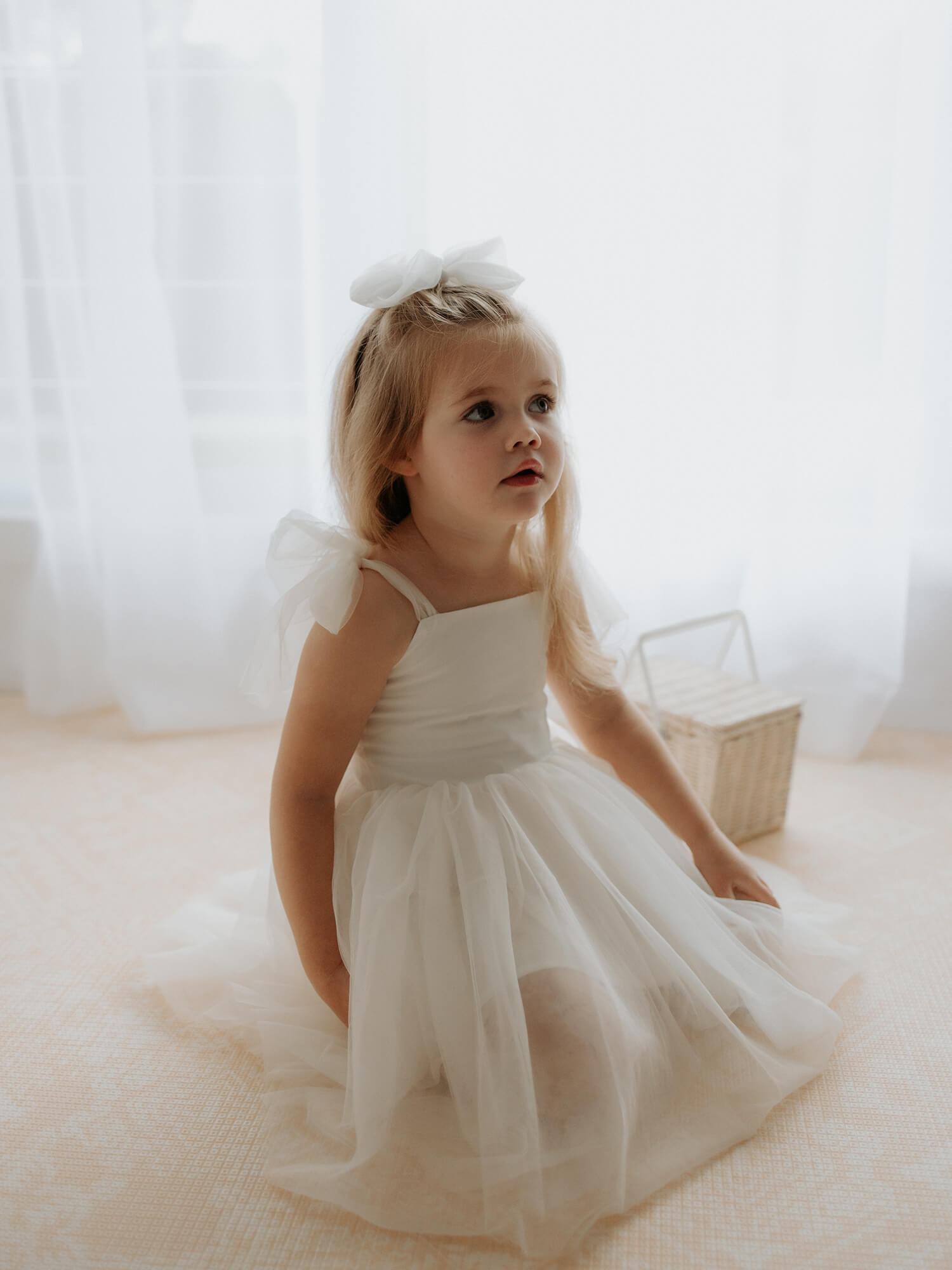 A young girl sits wearing our Harper tea length flower girl dress in cream.