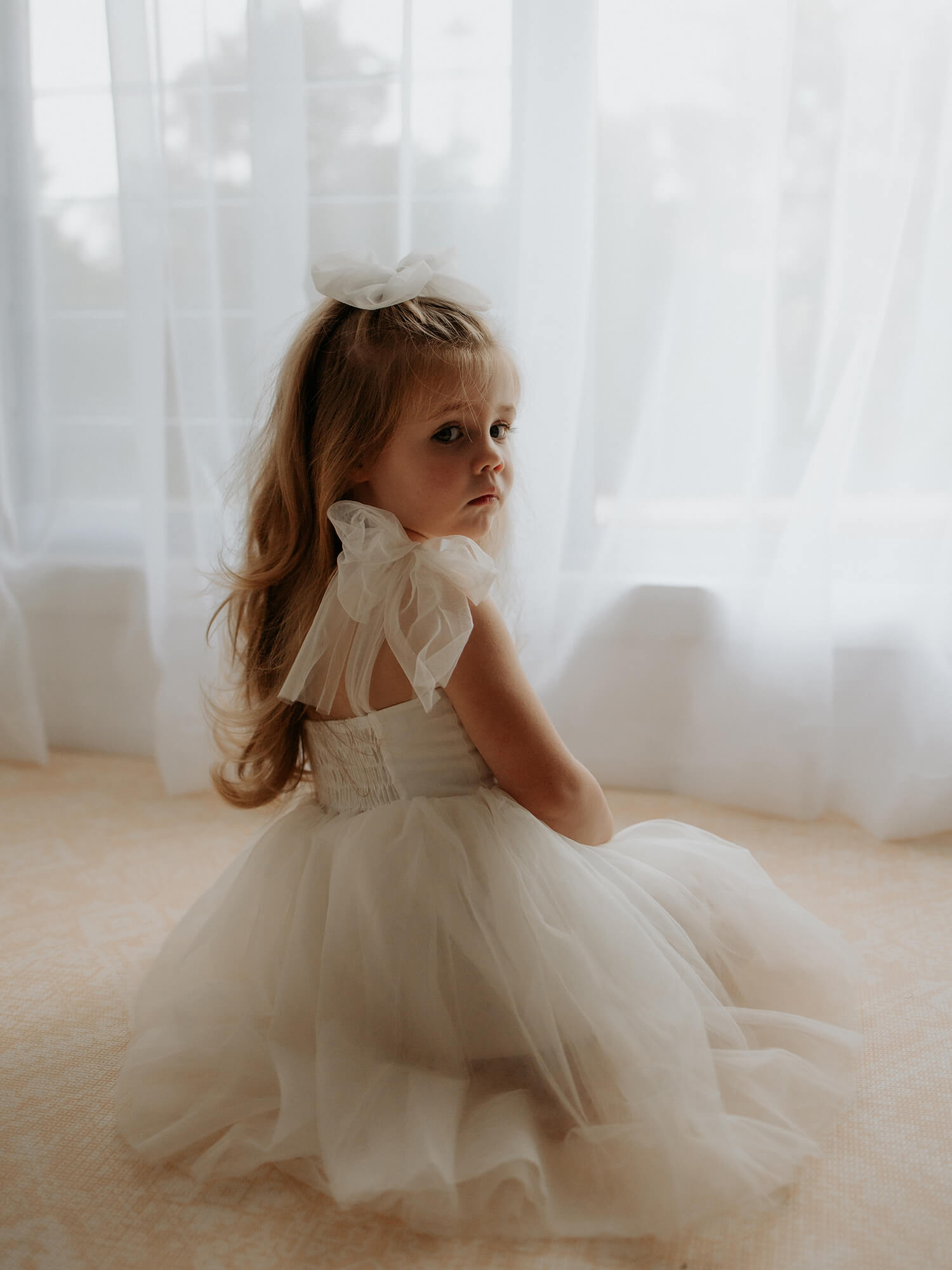 Flower girl wears our Harper cream tea length flower girl dress with tulle tie straps.