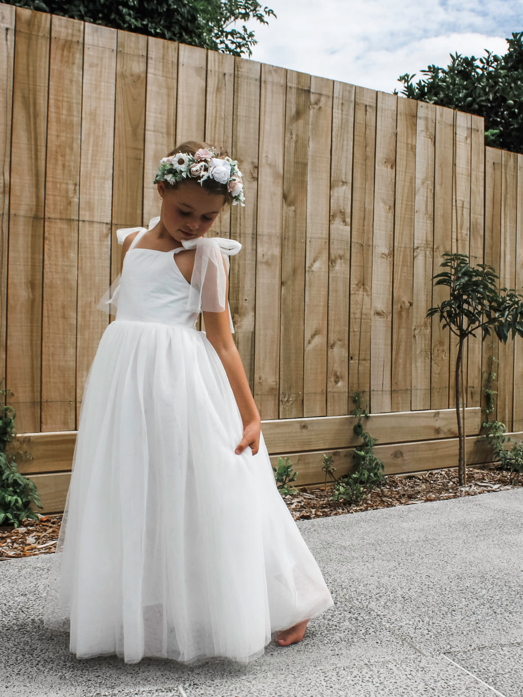 Harper flower girl dress worn by a young girl. Soft tulle skirt and straps with a shirred bodice. Worn with our Daisy flower crown.