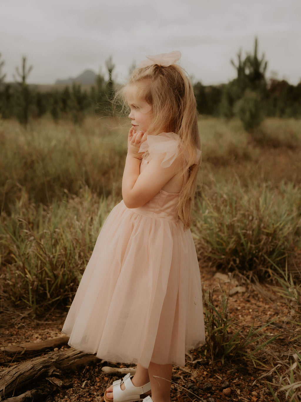 Isla champagne flower girl dress is worn by a young girl. She also wears a matching champagne tulle bow in her hair.