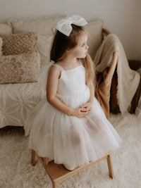 Isla tulle bow sleeve flower girl dress in ivory is worn by a young girl, she also wears a large ivory tulle bow in her hair.