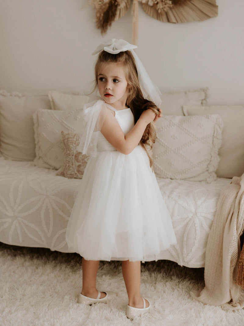 Isla white flower girl dress is worn by a young girl, she also wears a matching tulle bow in her hair.