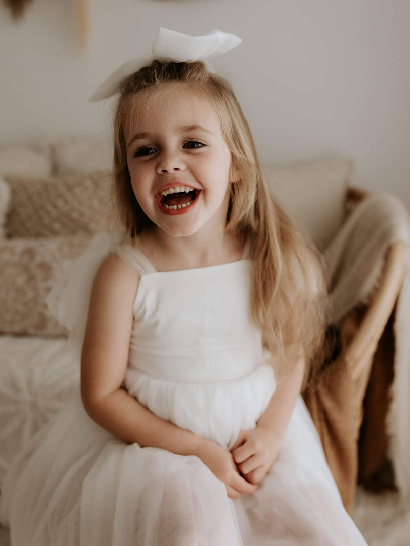 A young girl laughs wearing our Isla light ivory flower girl dress and large tulle bow hair clip.