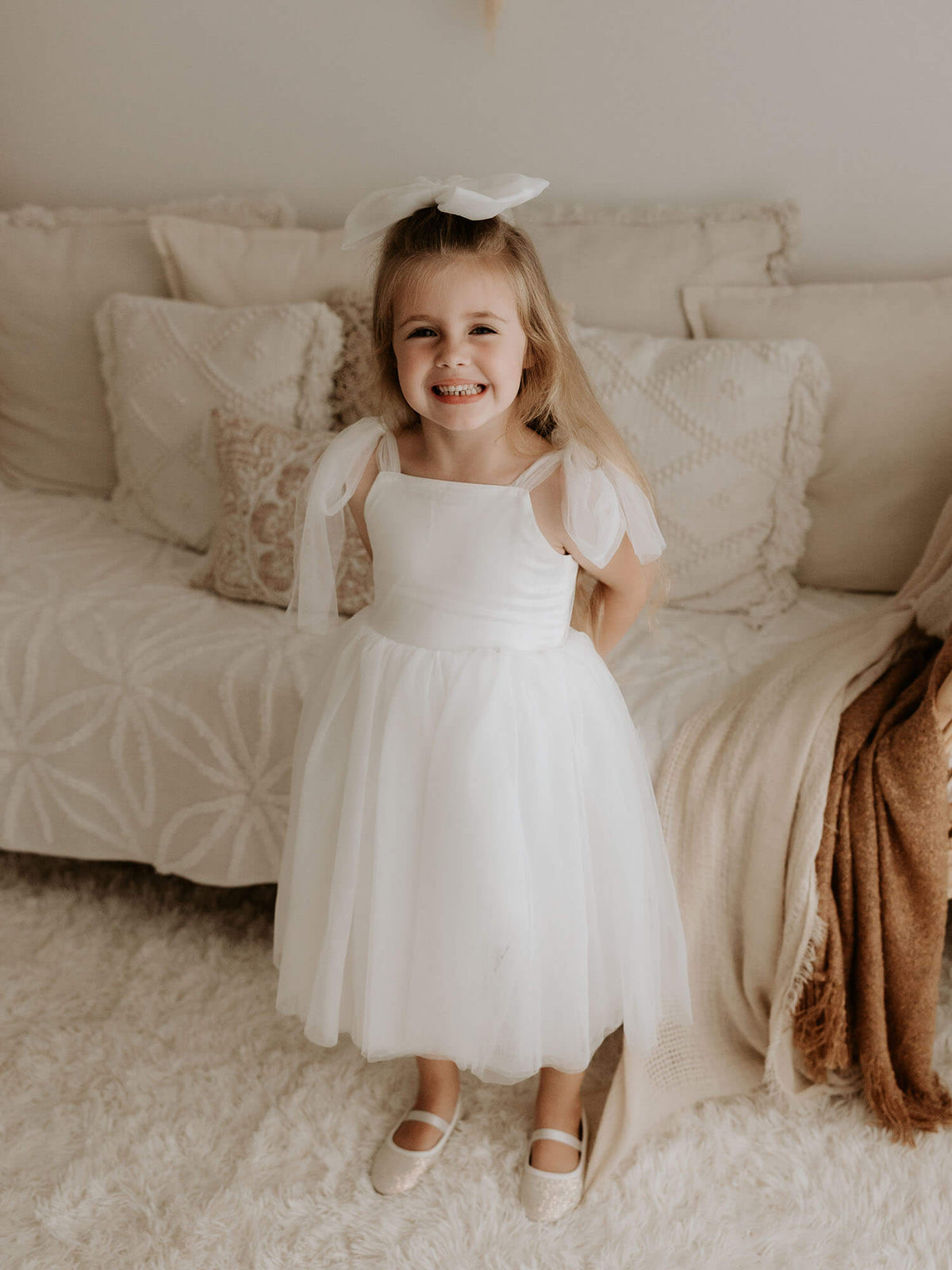 A young girl smiles wearing our Isla flower girl dress in light ivory.