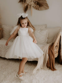 Twirling little girl wears our Isla flower girl dress in ivory and large tulle bow hair clip.