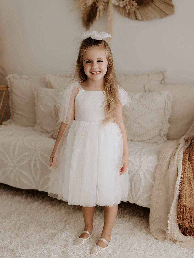 Isla flower girl dress in light ivory is worn by a young girl. She also wears our large ivory tulle bow in her hair.