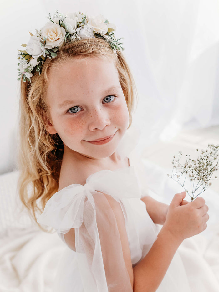 A young girl smiles wearing our Callie ivory flower headband and Isla flower girl dress.