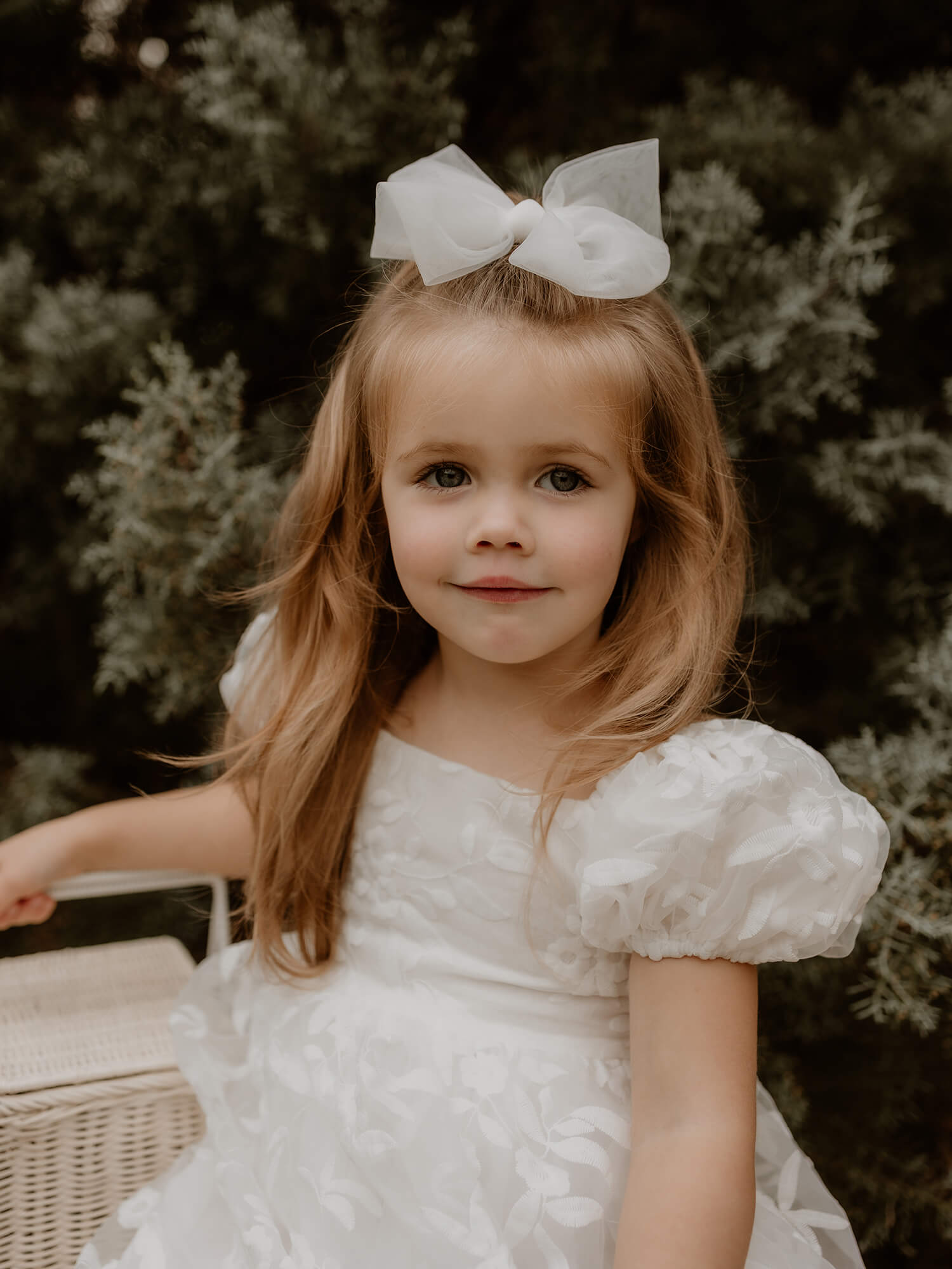 Puff sleeve flower girl dress is worn by a young girl holding a flower girl basket. She also wears a tulle bow hair clip.