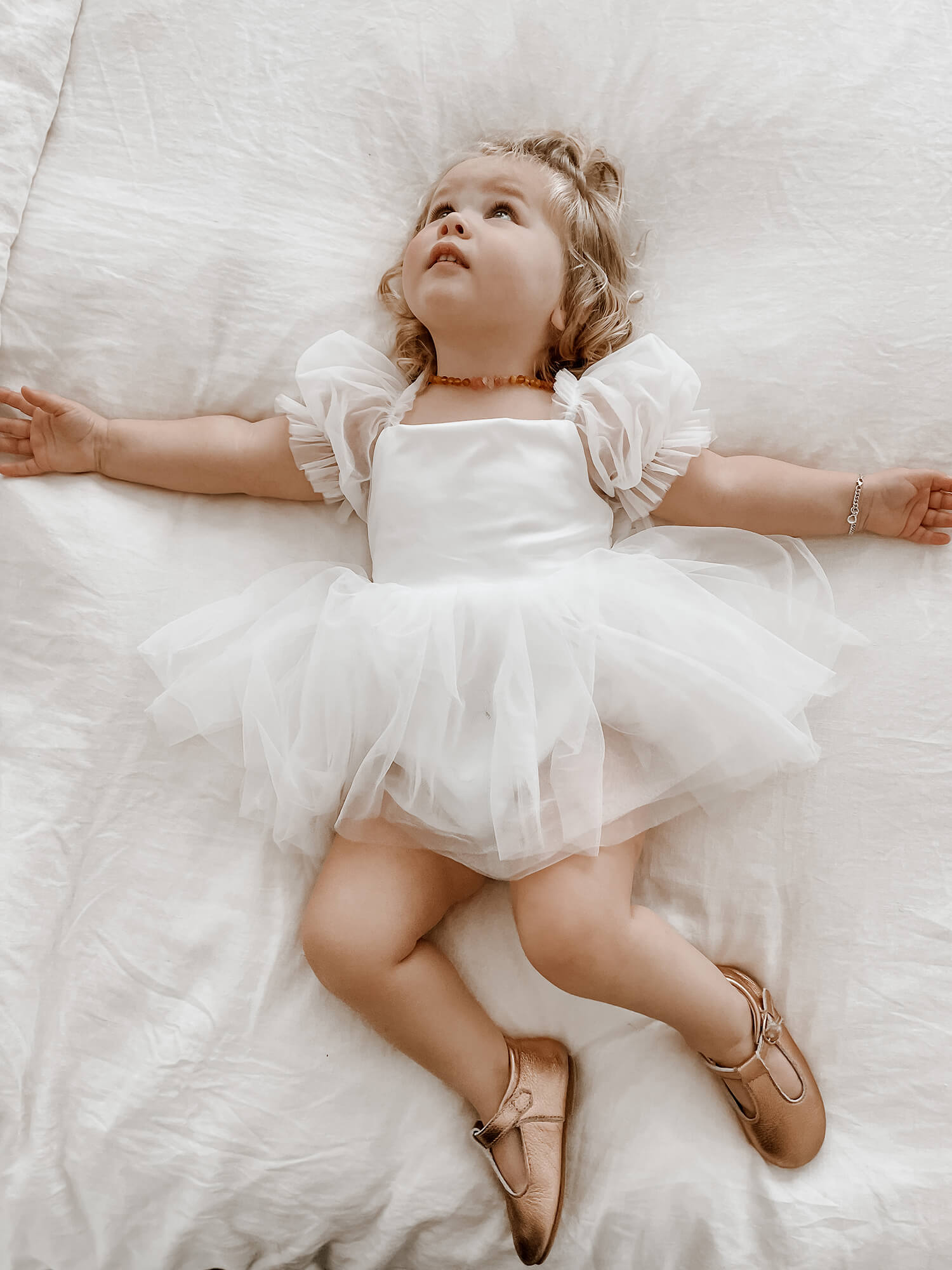 Toddler girl wears our Layla tulle puff sleeve flower girl romper, showing the matte satin bodice and tulle puff sleeves.