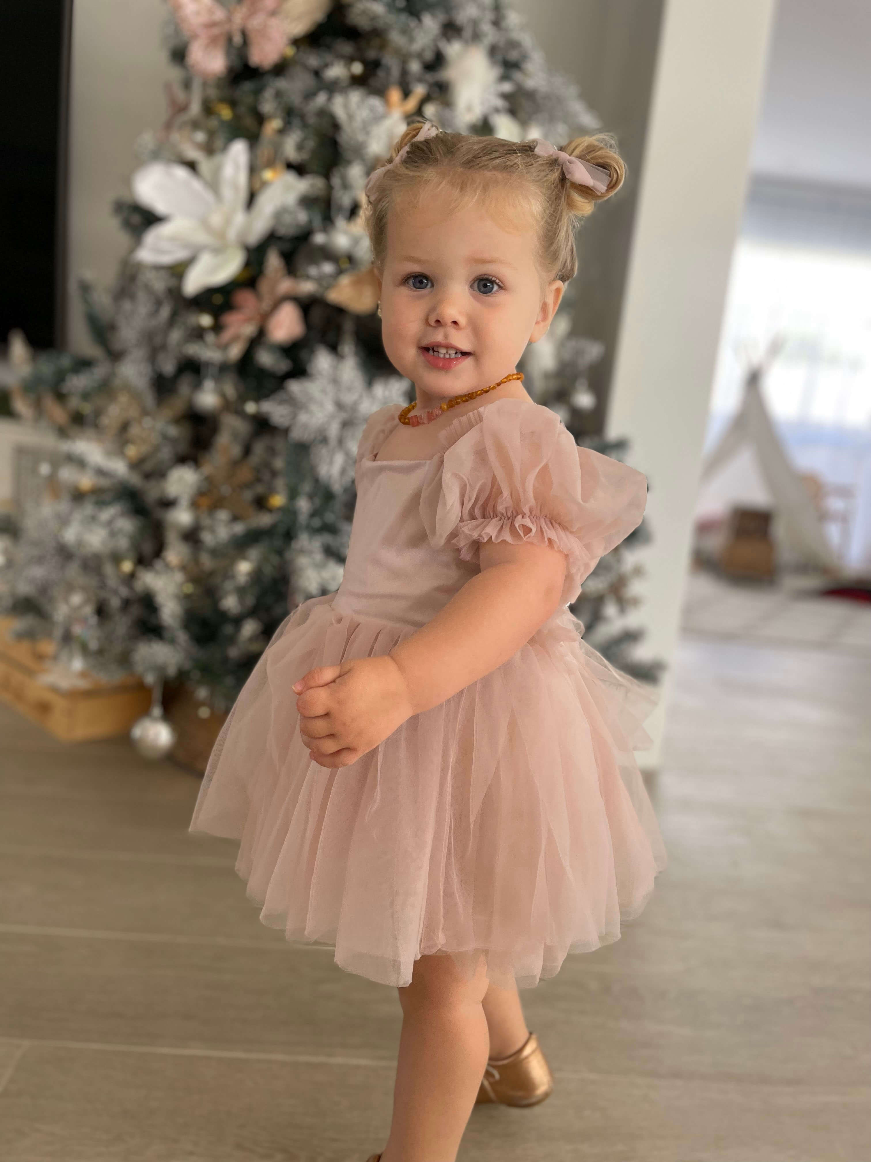 A toddler with tulle pigtail bows in her hair wears our Layla dusty pink flower girl dress.