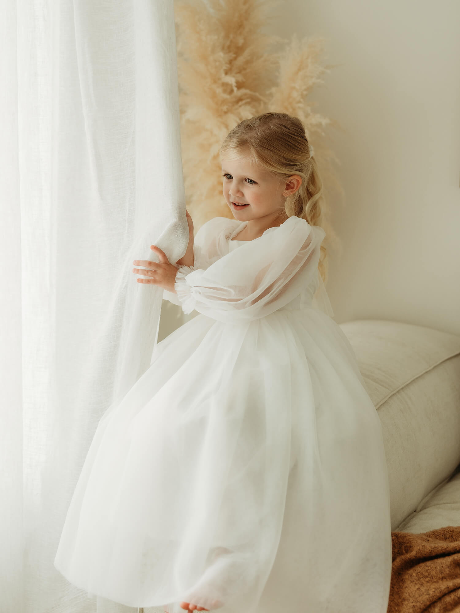 Wren ivory full length flower girl dress is worn by a young girl, showing the full length tulle sleeves and skirt.