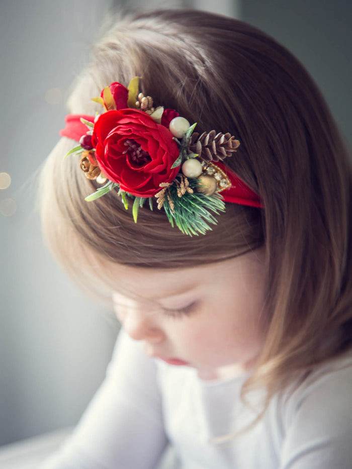 Chloe red Christmas floral headband shown on a toddler. A red centre peony surrounded with Christmas accents, including a mini pinecone and some gold. 
