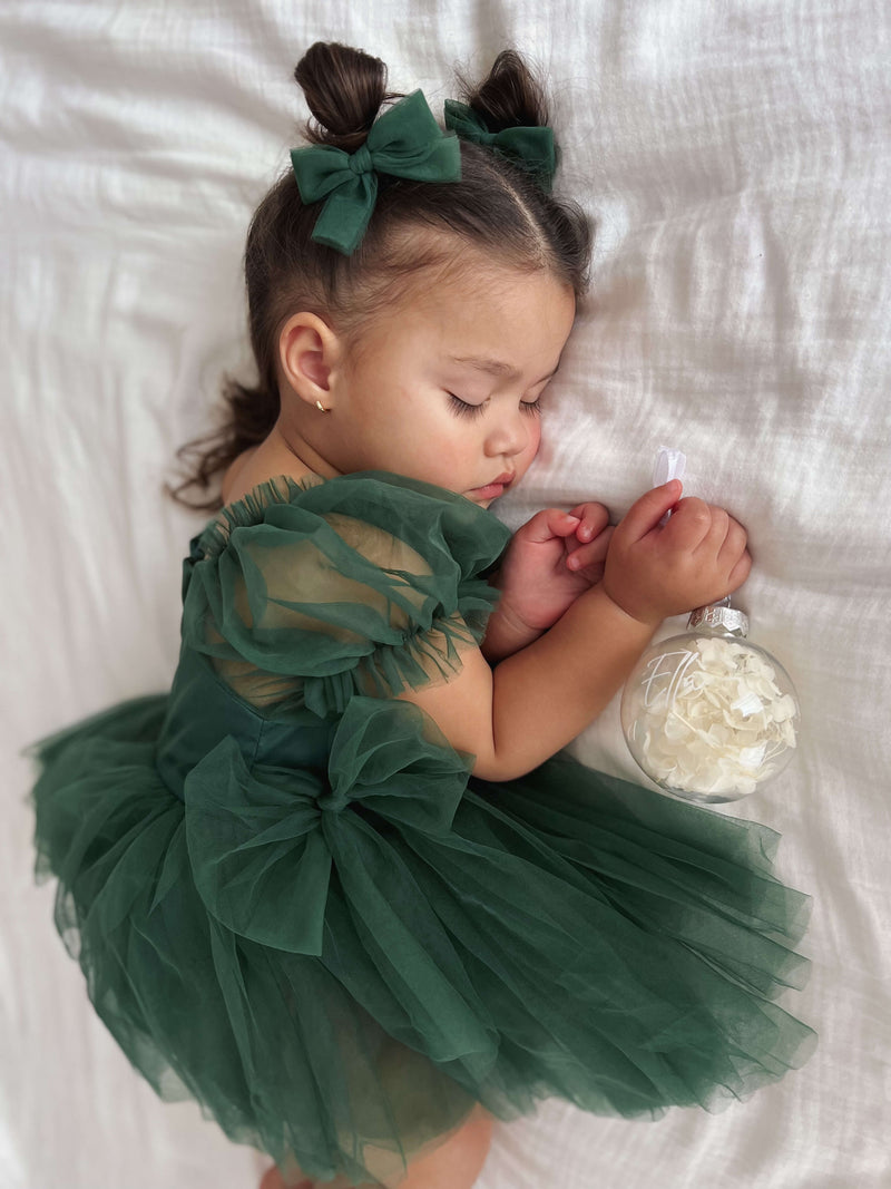 Clara emerald puff sleeve flower girl romper is worn by a sleeping baby. She also wears our emerald tulle pigtail bows in her hair.