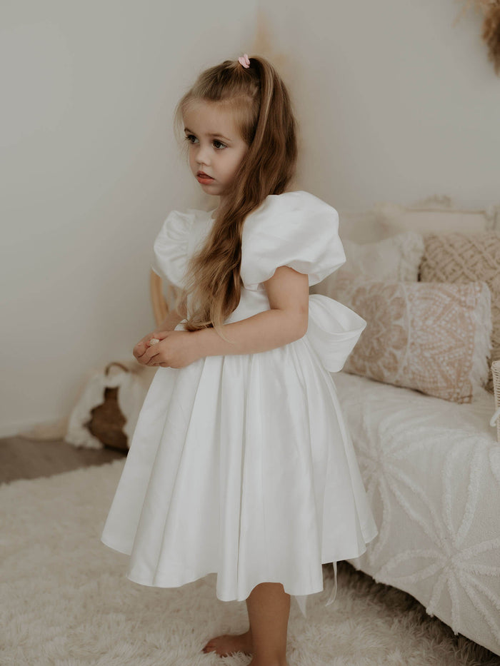 Frankie satin puff sleeve flower girl dress is worn by a young girl.