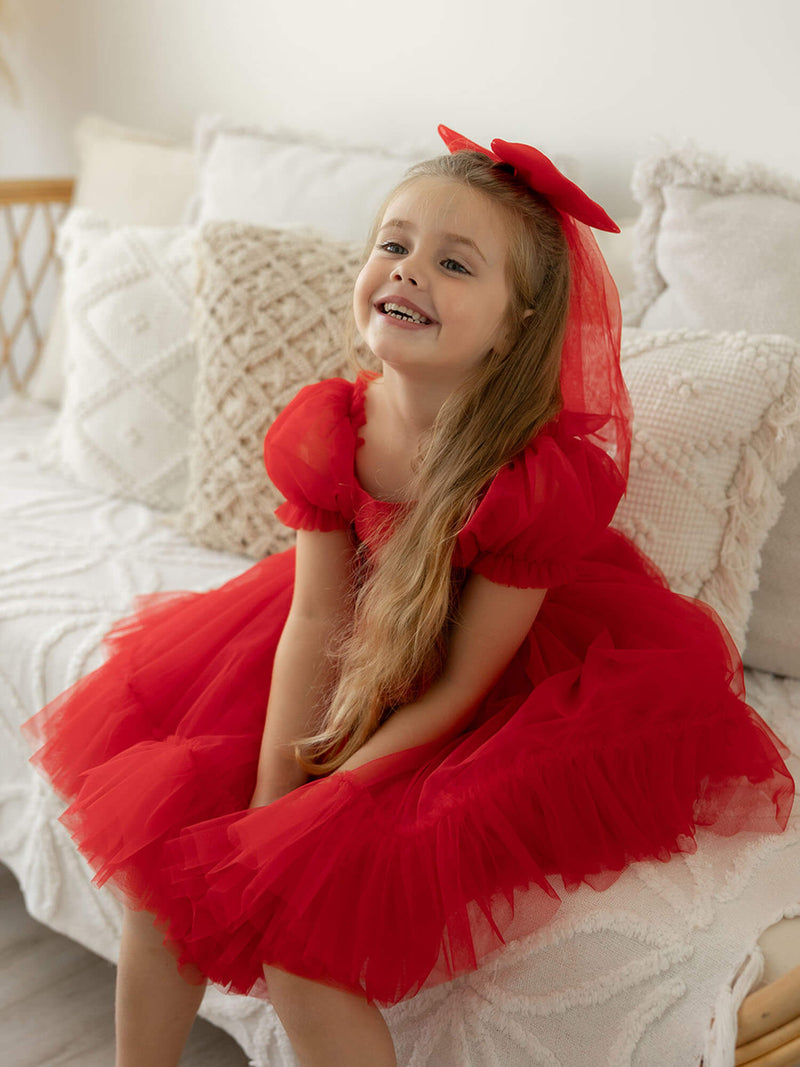 Gabrielle flower girl and Christmas dress in ruby red is worn by a young girl, she also wears a matching large tulle bow.