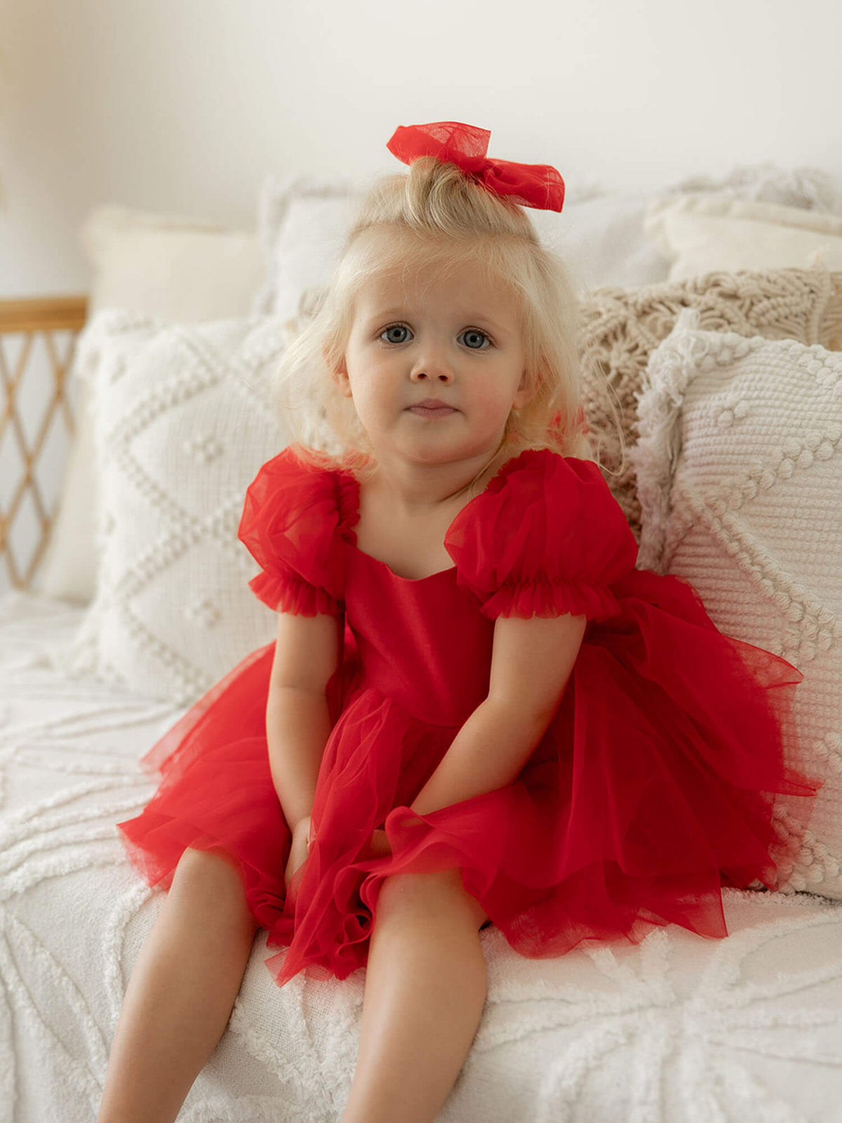 A toddler sits wearing our Gabrielle red flower girl and Christmas romper, and matching tulle hair bow.