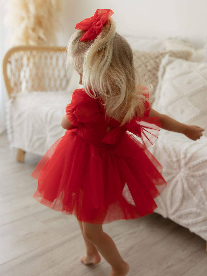 Gabrielle ruby red baby flower girl dress and Christmas dress is worn by a toddler who is twirling. It has a tulle bow at the back.