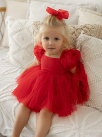 Gabrielle red Christmas baby romper is worn by a toddler, she also wears a red tulle hair bow.