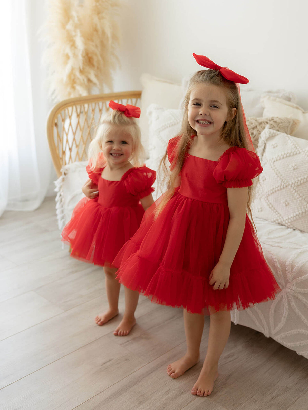 Sisters wearing matching tulle puff sleeve flower girl dresses & Christmas dresses in ruby red.