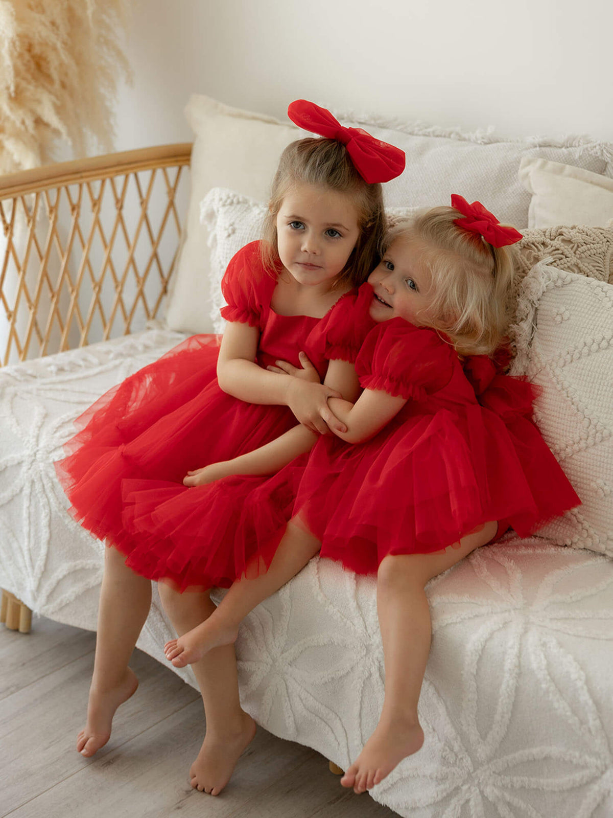 Matching sister Christmas dresses are worn by two young sisters sitting on a couch.