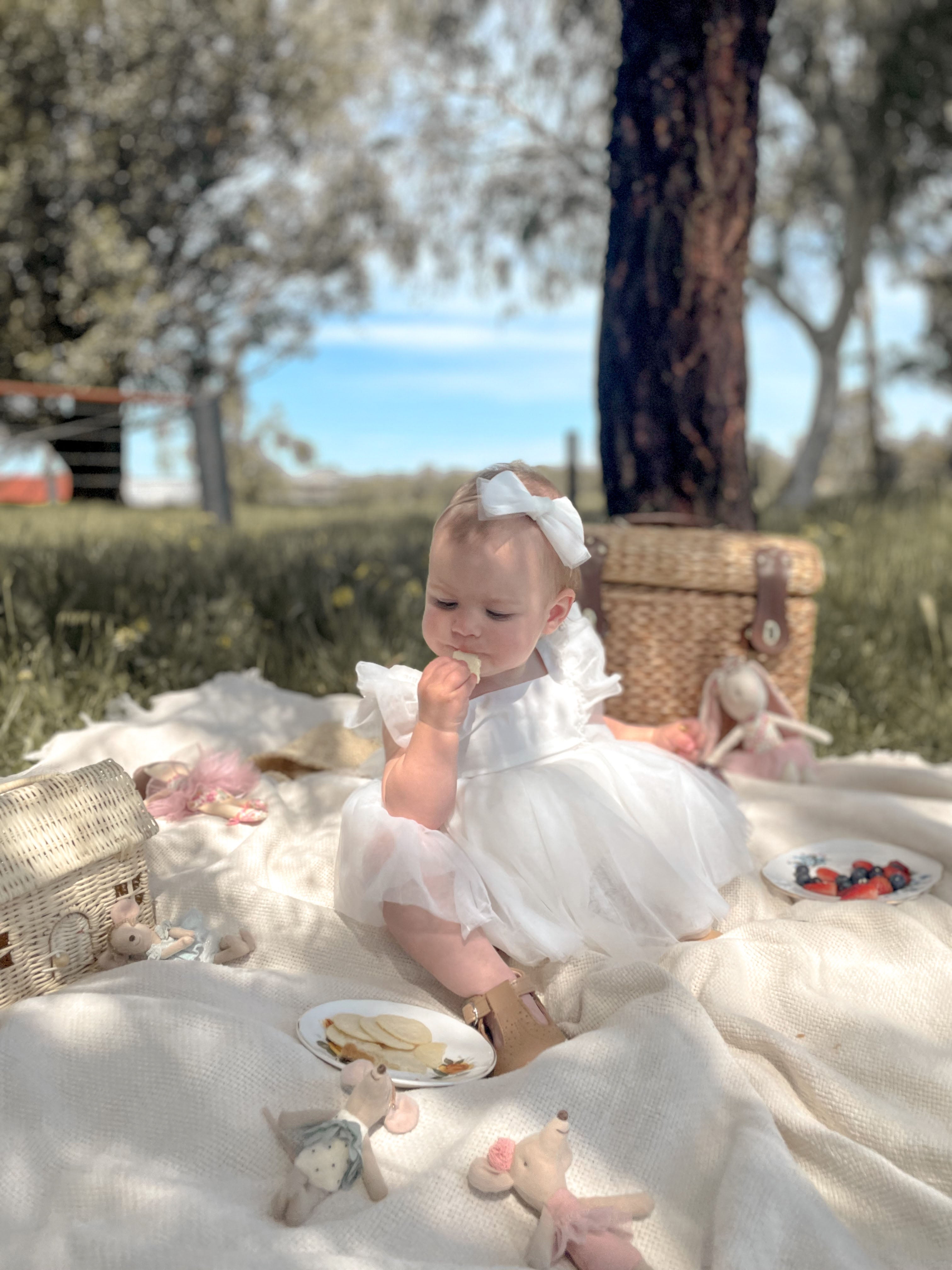 A baby sits wearing our Gigi baby flower girl romper and ivory tulle bow headband.