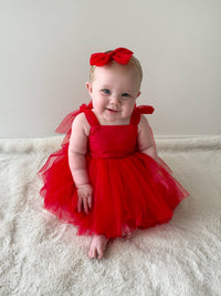 A baby smiles wearing our Harper Christmas romper dress in ruby red and matching tulle bow headband.